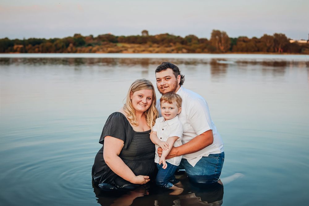 Family portrait at sunset with calm lake water in background. Maternity photography