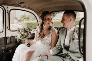 Pasgetrouwd stel zit in hun trouwauto en lachen naar elkaar