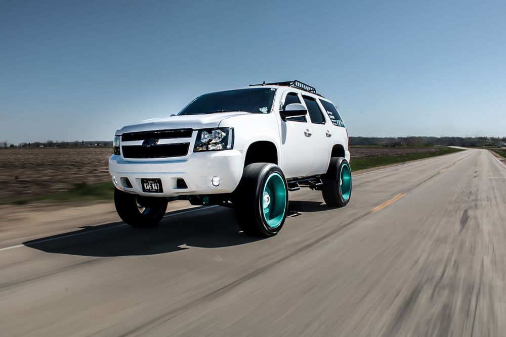 White Chevrolet Tahoe with turquoise wheels driving on an empty road.