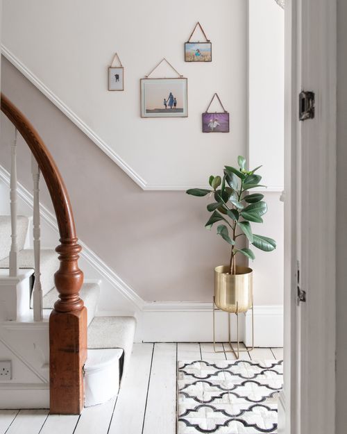 White hallway with wooden banister, geometric rug, and framed artwork showcases modern farmhouse style decor.
