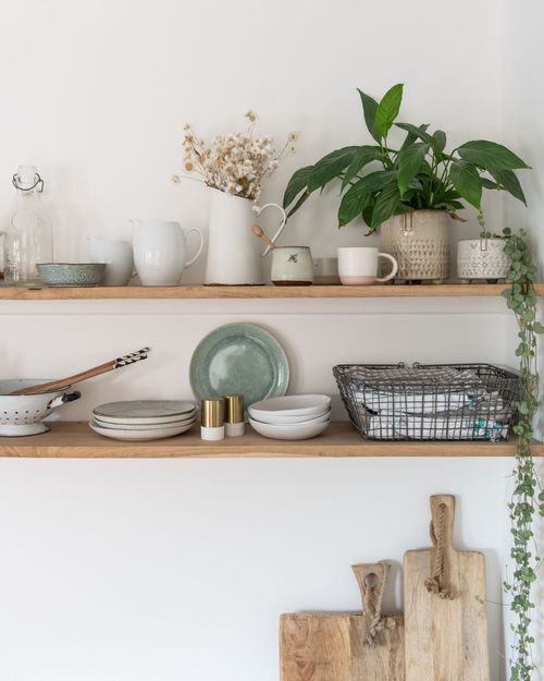 Rustic open shelving displays white dishes, glassware, and potted plants against a white wall with natural wood accents.