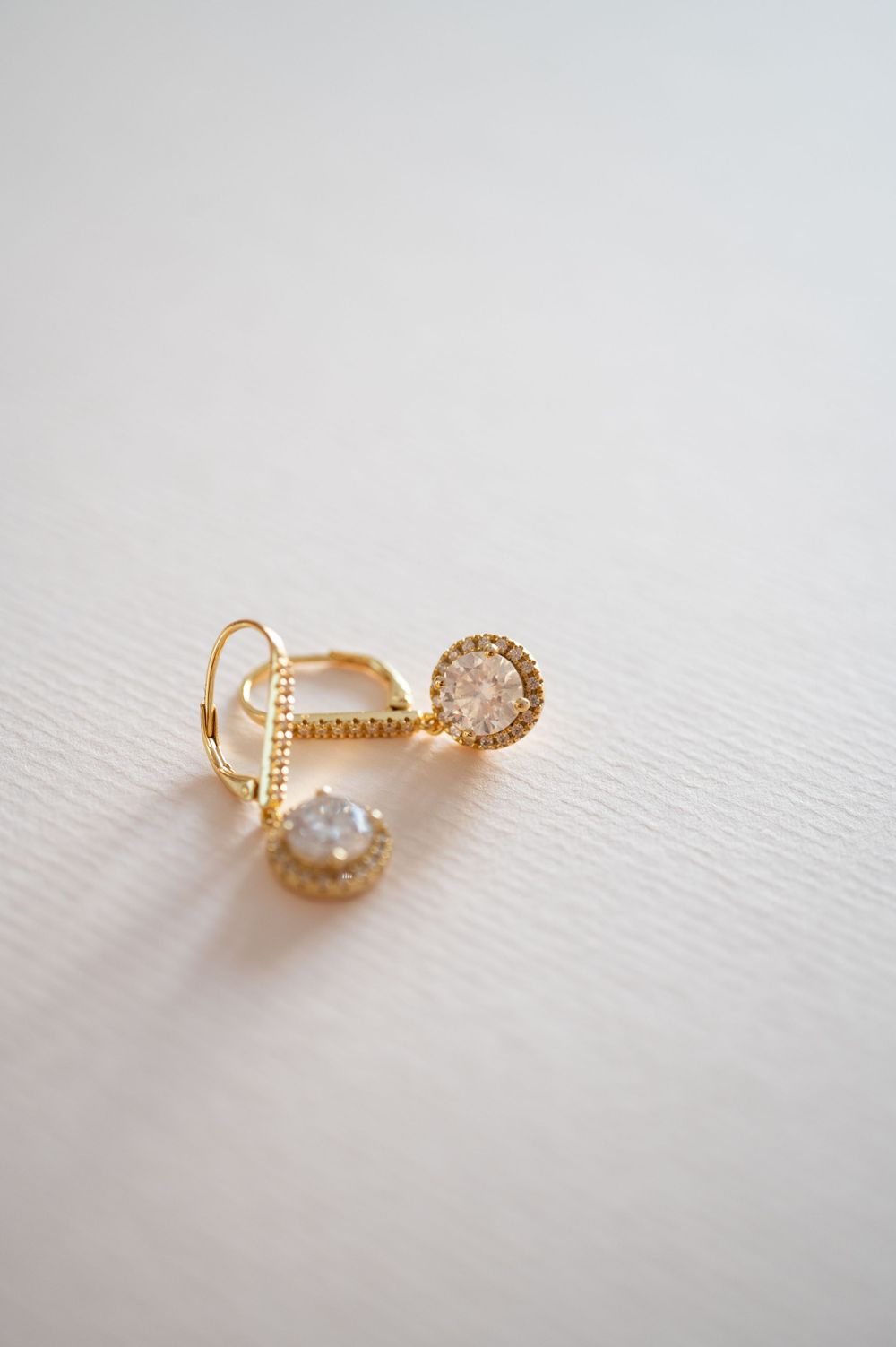 Delicate gold earrings with small druzy crystal details photographed on a white textured surface.