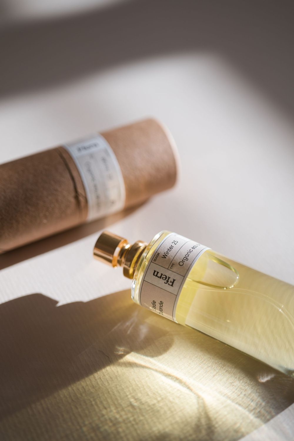 A close-up view of a perfume bottle lying on a textured white surface in warm lighting.