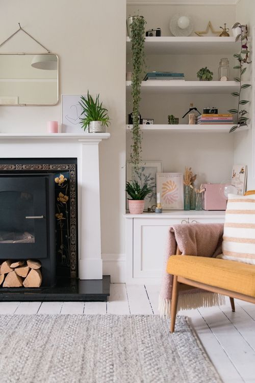 Modern minimalist living room with white walls, wooden flooring, open shelving, and a cozy seating area near a fireplace.