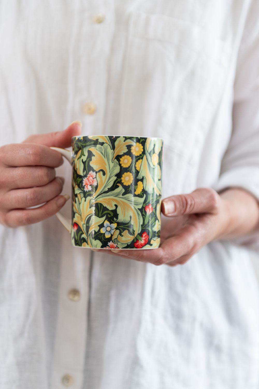 Person holding a green and yellow botanical patterned ceramic mug.