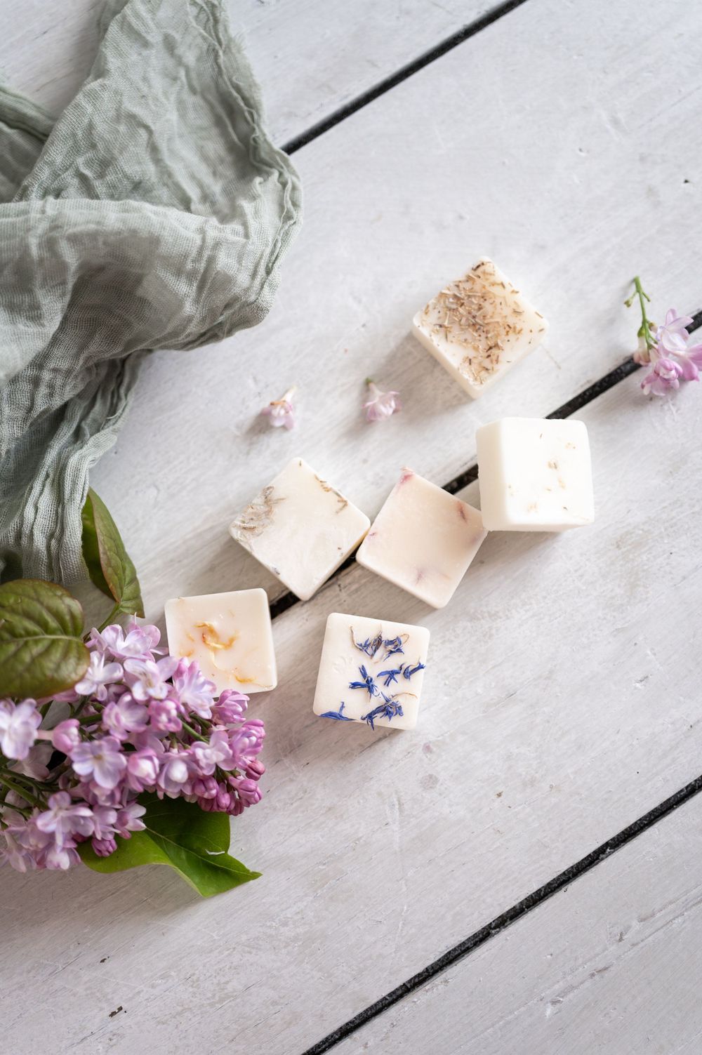 Pink and purple lilac flowers with sage green leaves arranged with beige paper on white wooden planks.