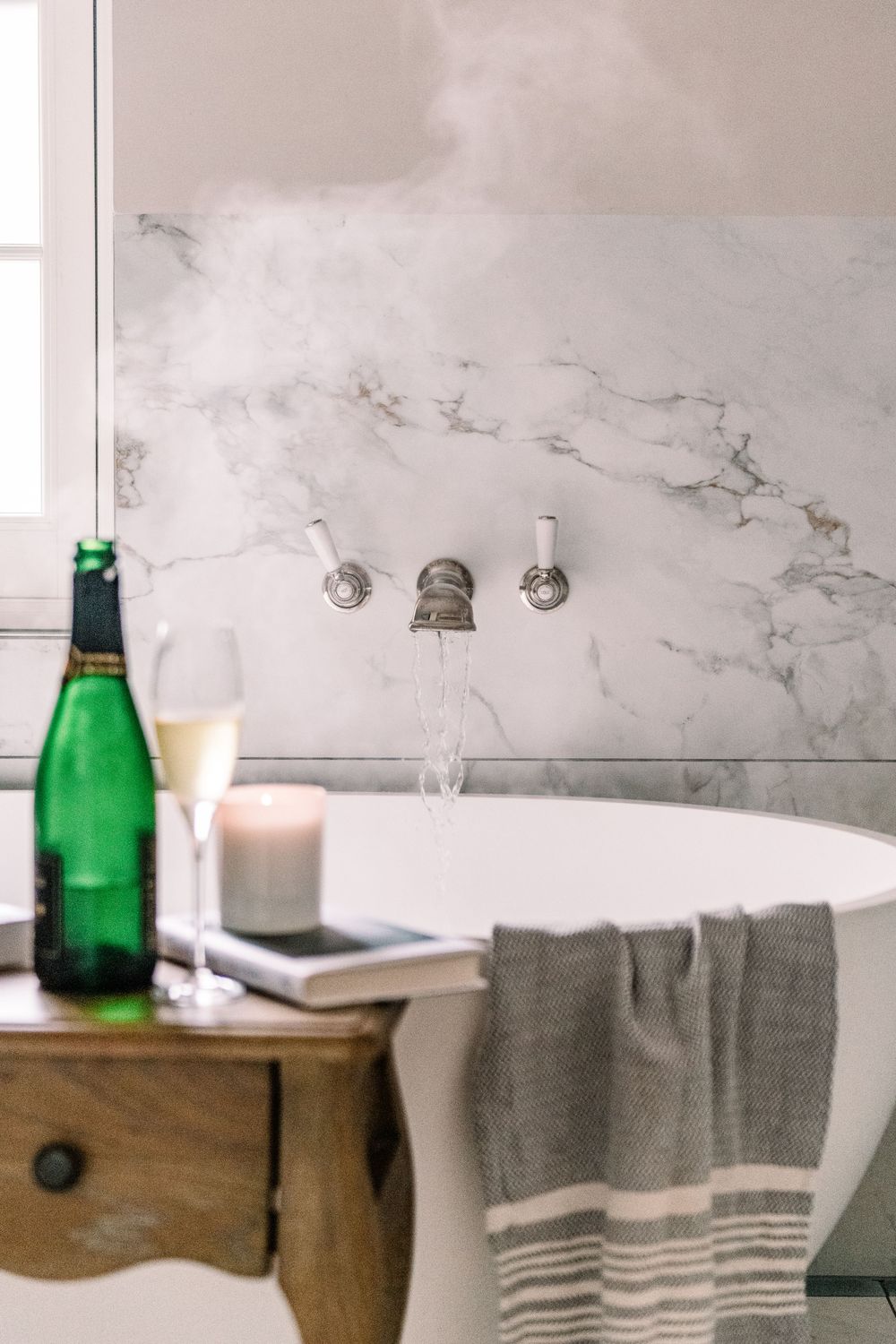 Modern restaurant table setting with marble wall, wooden table, gray striped linens and green glass water bottle.