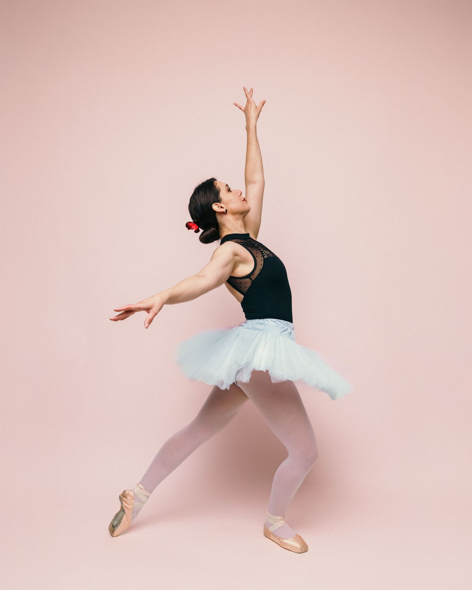 Ballet dancer in tutu and pointe shoes performs graceful pose against pink backdrop.