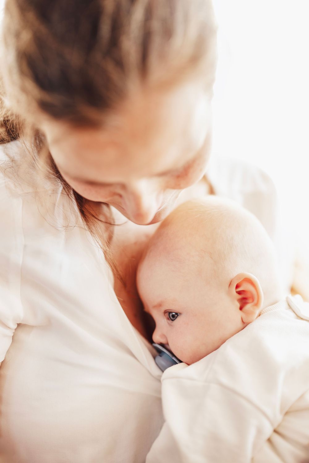 A tender moment shows a parent in white clothing holding and bonding with their infant baby.
