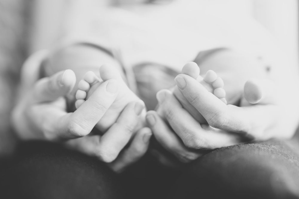 A black and white macro shot of small hands holding larger hands in an intimate tender moment.