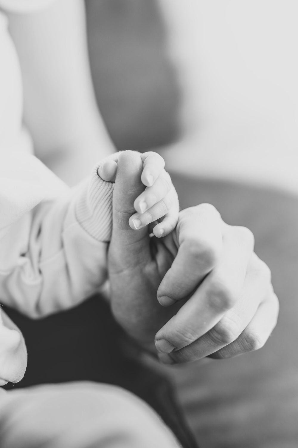 A tender black and white close-up of an adult's hands gently holding a baby's tiny foot.