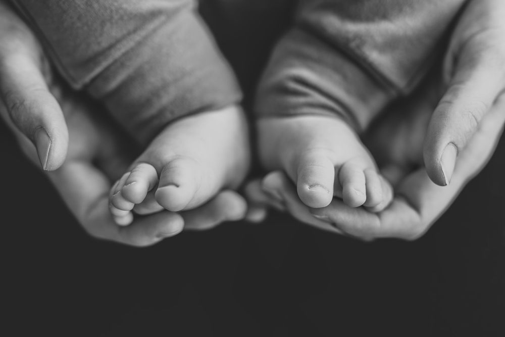 Adult hands gently hold tiny baby feet in black and white close up photograph.