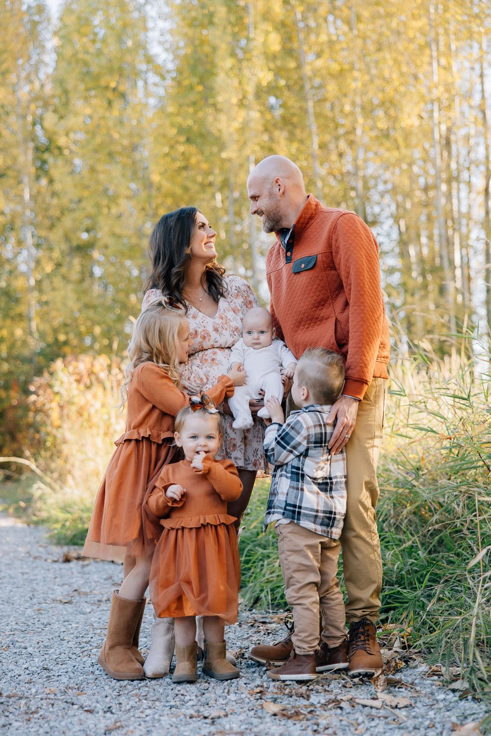 Family wearing coordinated autumn outfits posing on gravel path with golden aspen trees in background.