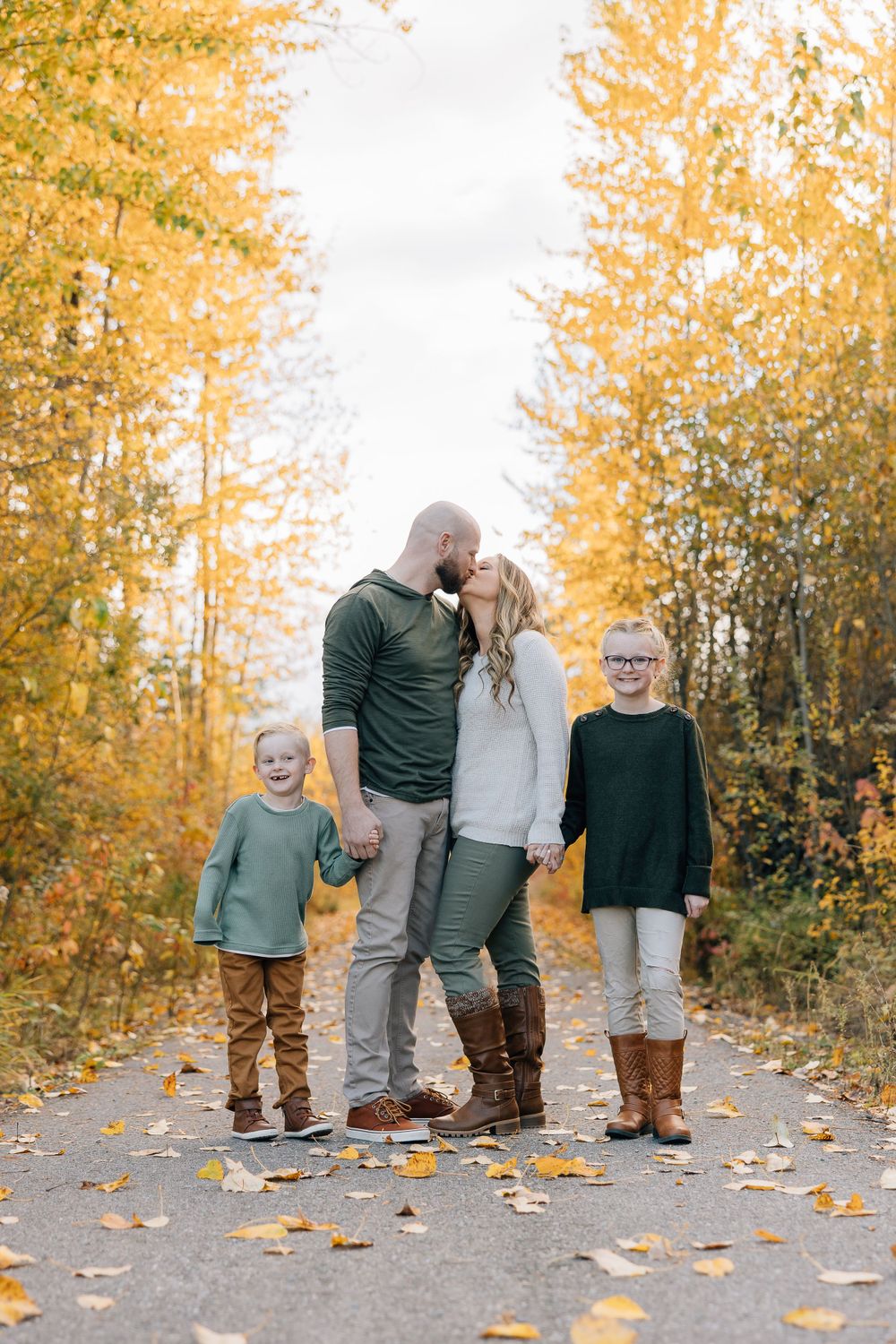 A group embraces on a leaf-covered path with golden autumn trees surrounding them on a cloudy fall day.