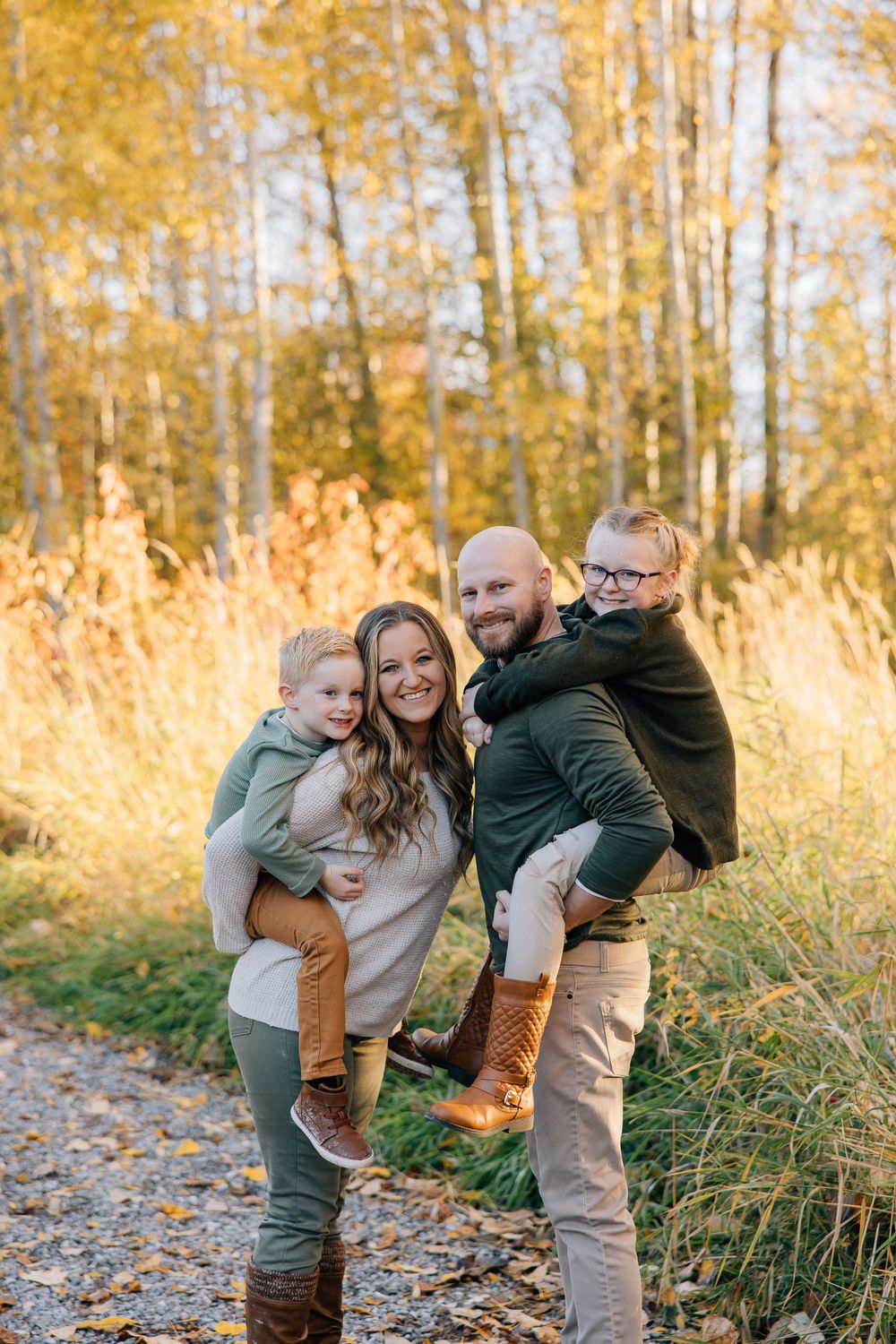 A family enjoys an autumn photoshoot together on a path surrounded by golden aspen trees and tall grasses.