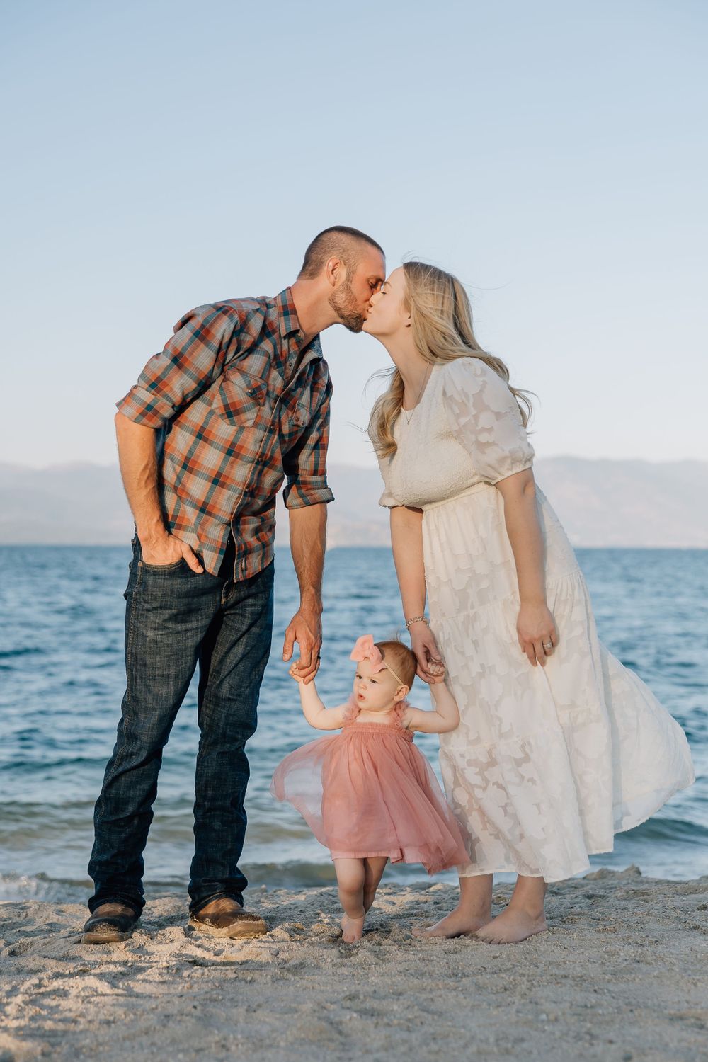 Family shares intimate moment on beach with mountains and ocean in background.