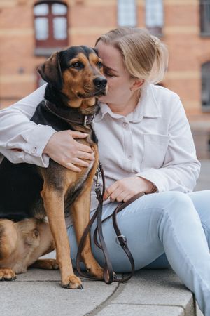 Mensch-Hund-Fotografie: Frau sitzt mit ihrem Hund vor einer Backsteinfassade, aufgenommen im Stadtgebiet von Dachau.