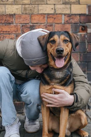 Mensch-Hund-Fotografie: Person sitzt auf dem Boden und hält ihren Hund im Arm, ruhige Aufnahme im urbanen Umfeld von München.