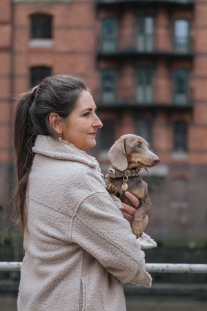 Mensch-Hund-Fotografie: Frau hält einen kleinen Hund im Arm und blickt zur Seite, fotografiert im Stadtgebiet von Freising.