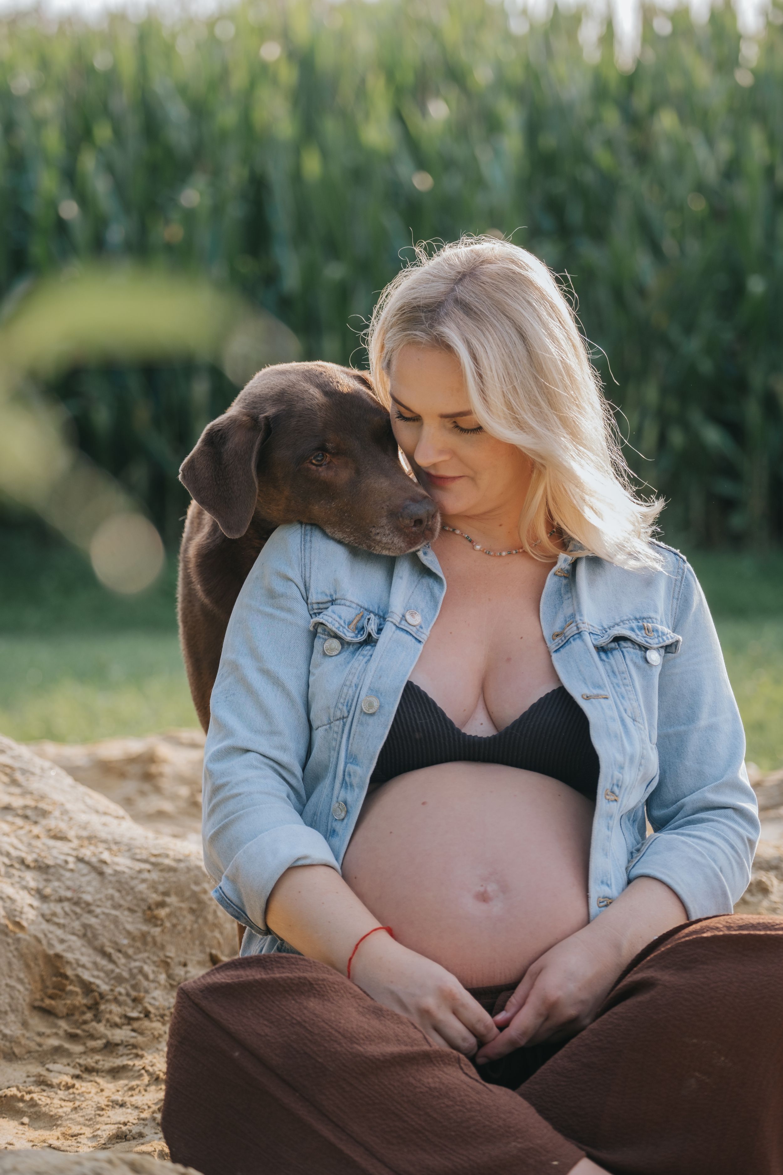 Familienfotografie: Schwangere Frau sitzt im Gras und blickt liebevoll zu ihrem Hund, natürliche Aufnahme im Raum Hohenkammer.