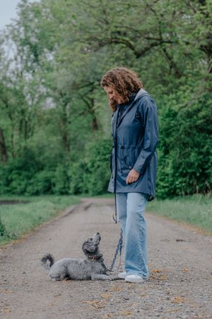 Mensch-Hund-Fotografie: Frau steht im Grünen neben ihrem sitzenden Hund, aufgenommen im Raum Hohenkammer.