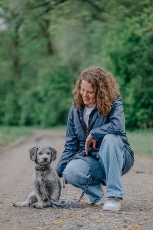 Mensch-Hund-Fotografie: Frau hockt neben einem Hund auf einem Weg im Grünen, ruhige Aufnahme im natürlichen Umfeld.