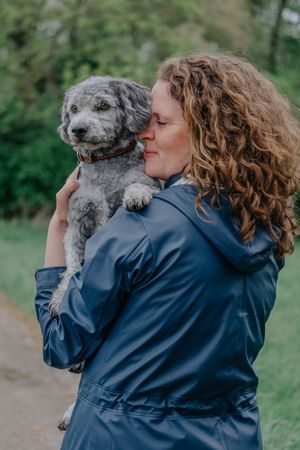 Mensch-Hund-Fotografie: Frau hält einen kleinen Hund im Arm und blickt über die Schulter, fotografiert bei Freising.