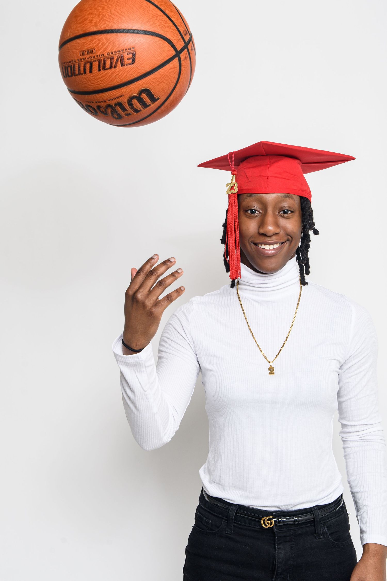 Graduate celebrating with colorful stars wearing black cap and gown with red stole at outdoor graduation ceremony.