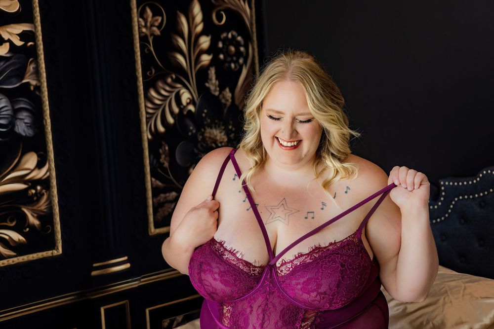 Romantic boudoir photography in burgundy lace against dark backdrop.
