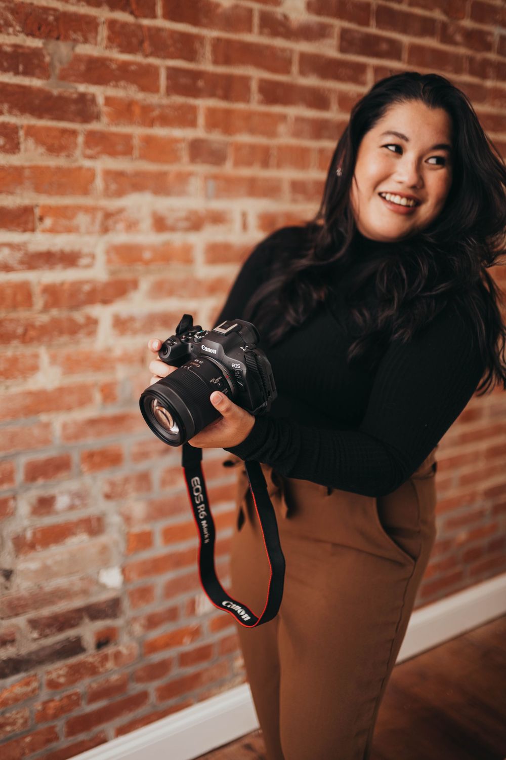 Person in black holding a camera against exposed brick wall background.