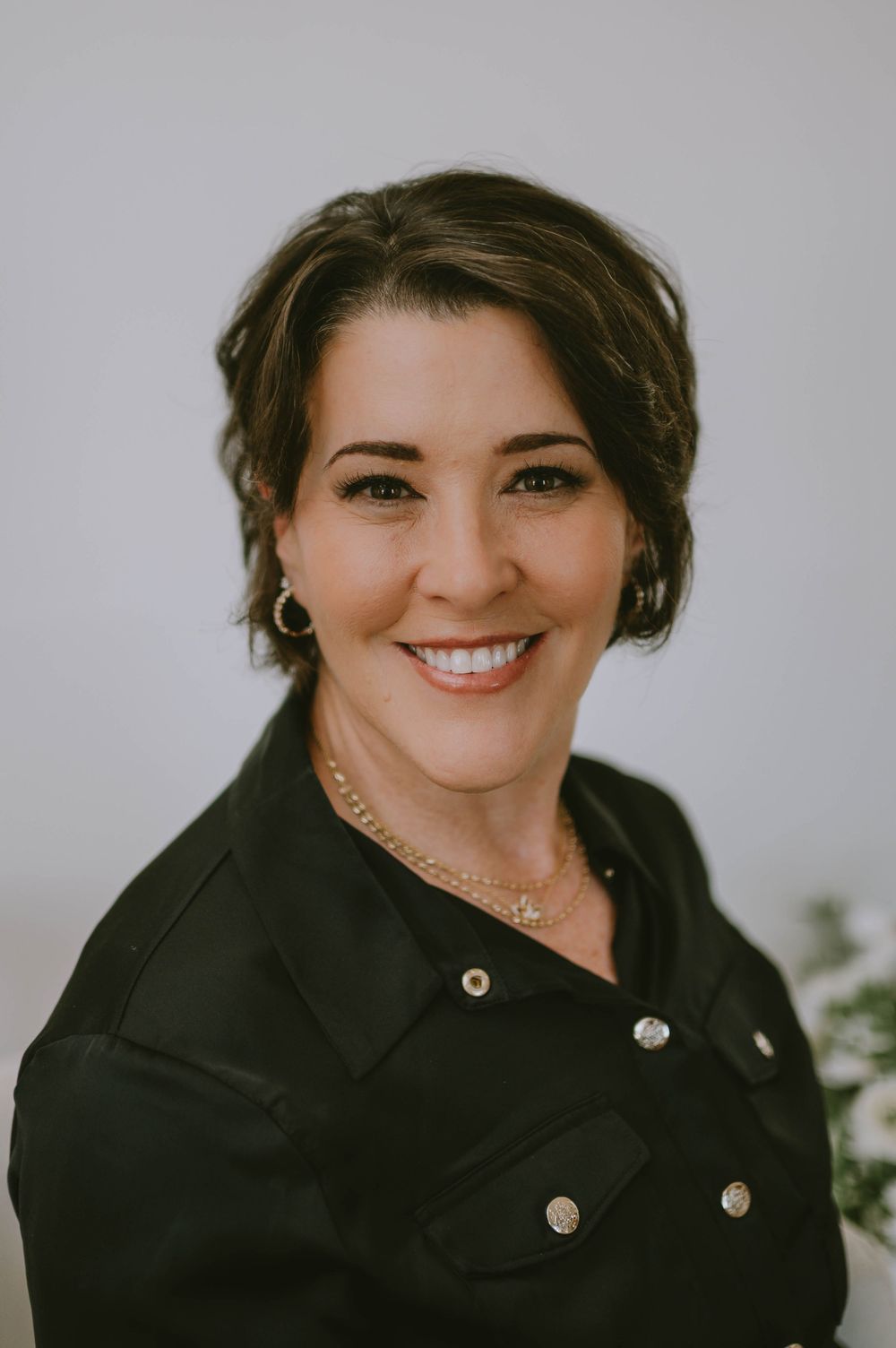 Professional headshot of someone wearing a black blazer with silver buttons against a light background.