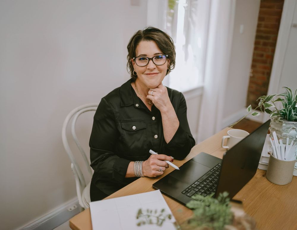 Casual business portrait showing someone working at a desk with laptop and plants.