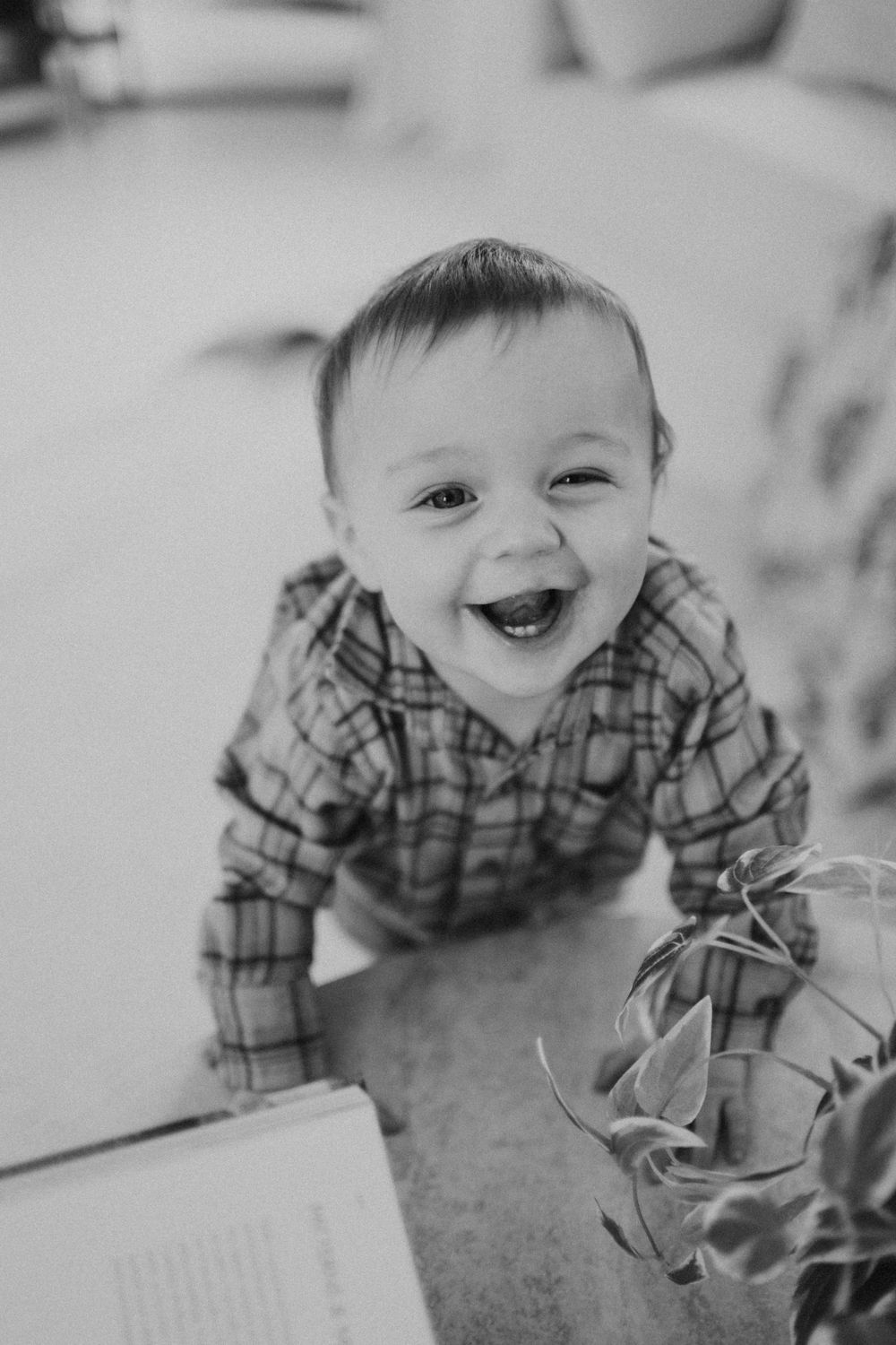Black and white photo of a happy laughing baby boy in a plaid shirt looking up at the camera.
