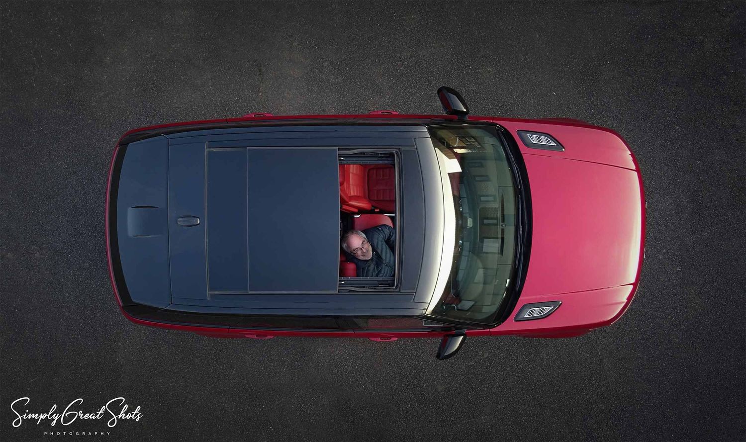 An aerial automotive photograph of Supercharged Range Rover with smiling man looking through the sunroof.