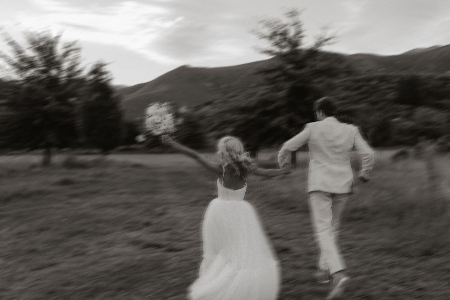Couple walking hand in hand through a desert landscape at sunset in wedding attire.
