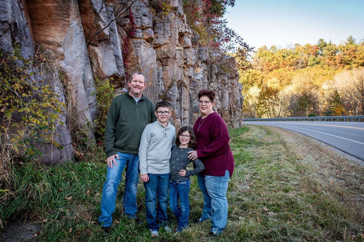 Three people posing by a rocky cliff face with a road in the background.