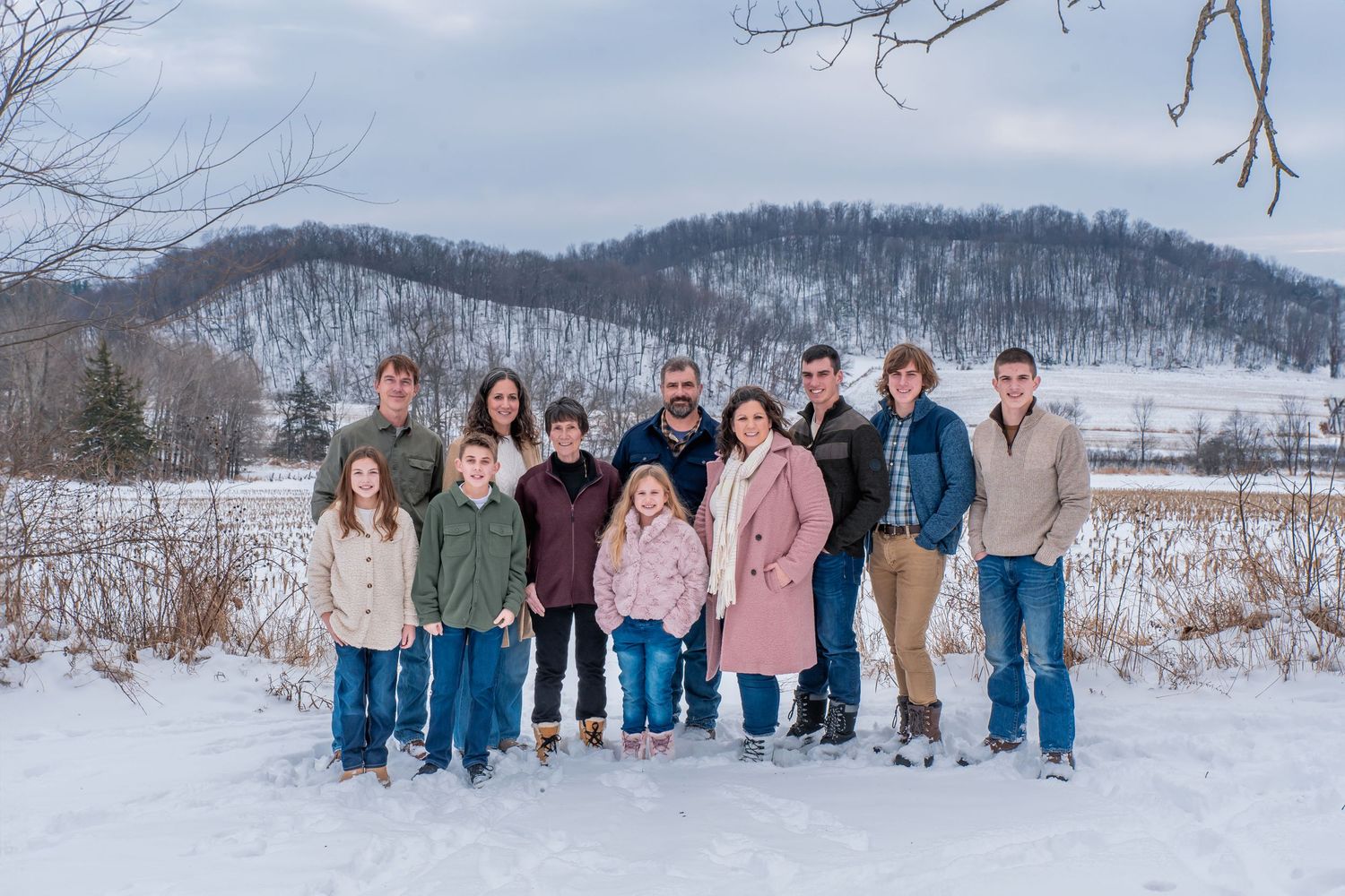 A group of people pose together in a snowy winter landscape with mountains and trees in the background.