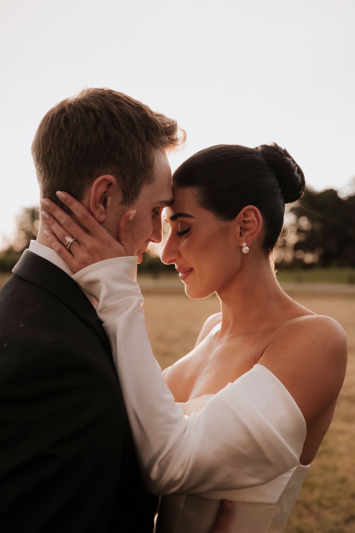 Intimate wedding portrait of couple in formal attire embracing during golden hour in an outdoor setting.