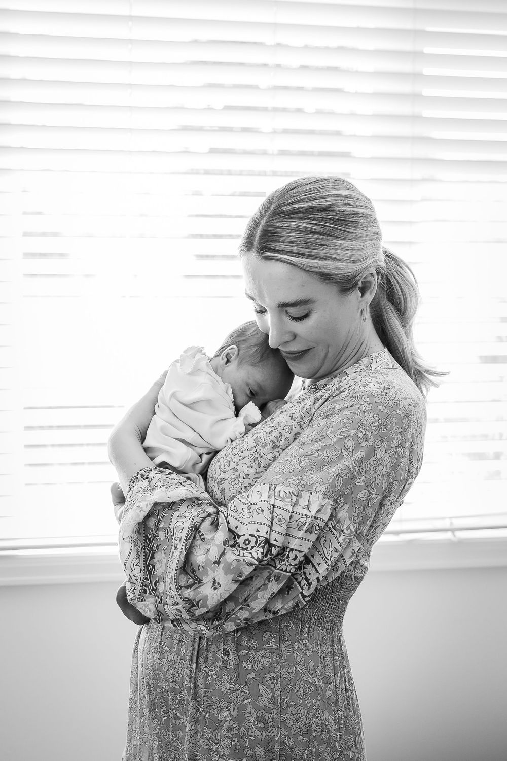 A new mother gently cradles her newborn baby at home in black and white image