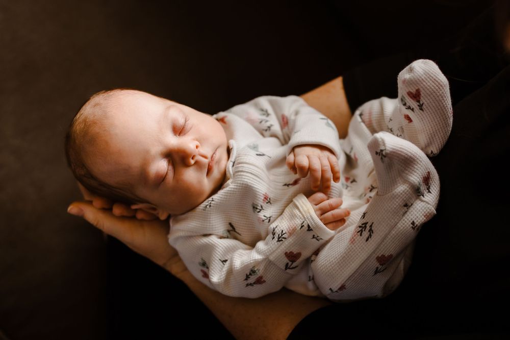 A parent gently holds their newborn baby in their arms, lit naturally in their home