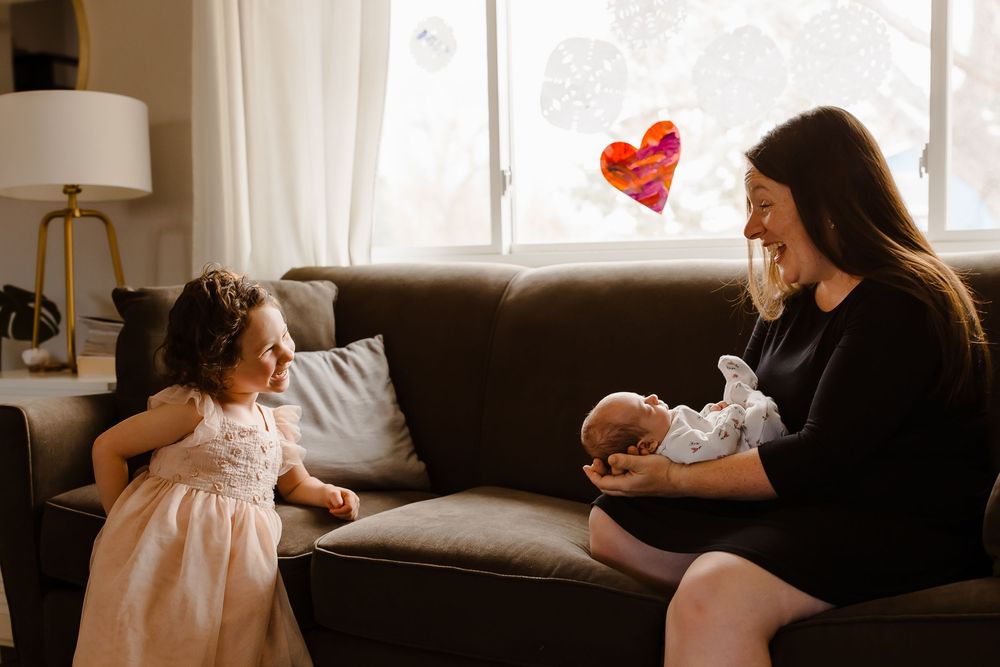 A candid interaction between a child and her mother holding a newborn baby in their home