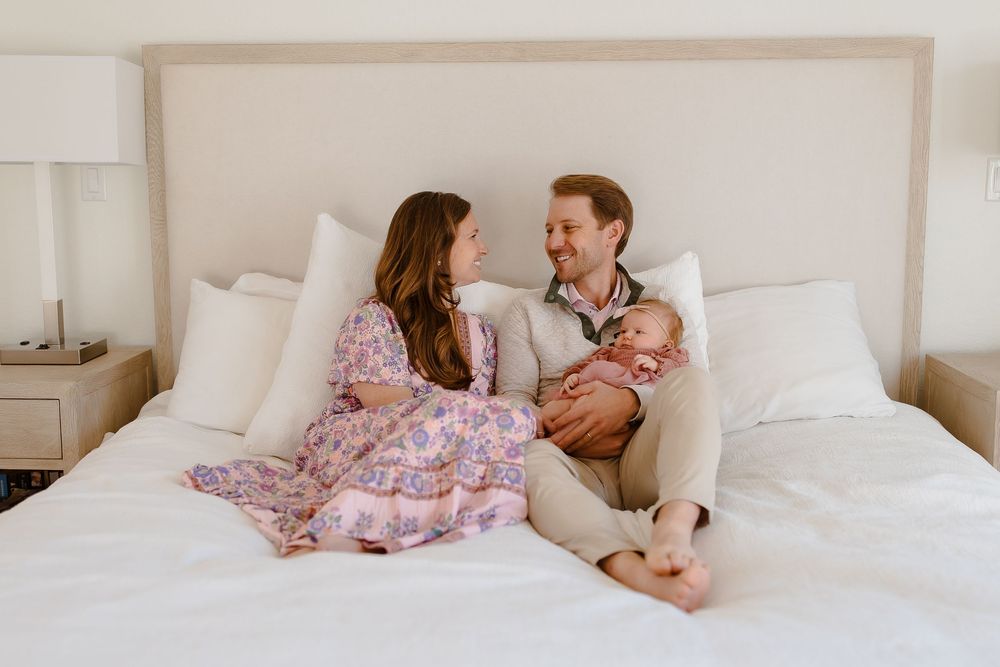 A family smiles naturally in their home with their newborn baby