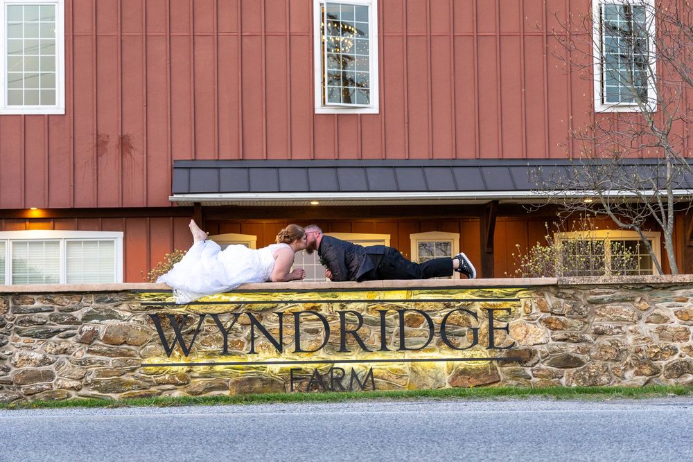 An illuminated sign for Wyndridge Farm mounted on a rustic stone wall beneath a red barn building.