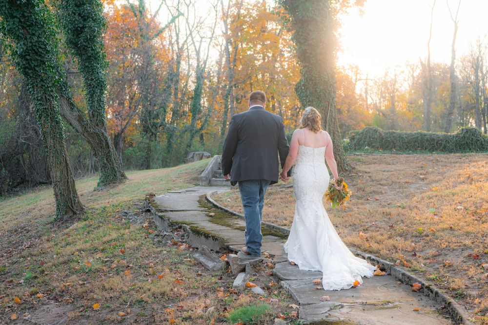 A couple walks hand in hand along a scenic autumn path surrounded by golden fall foliage and warm sunlight.