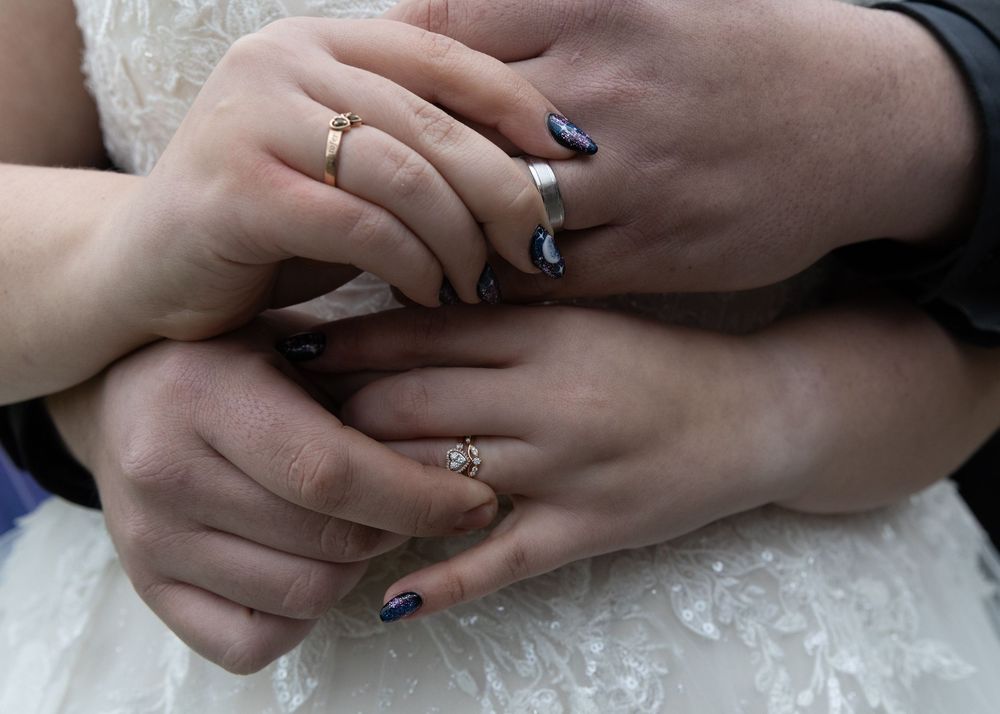Crossed hands with blue nail polish and silver rings resting on white fabric.