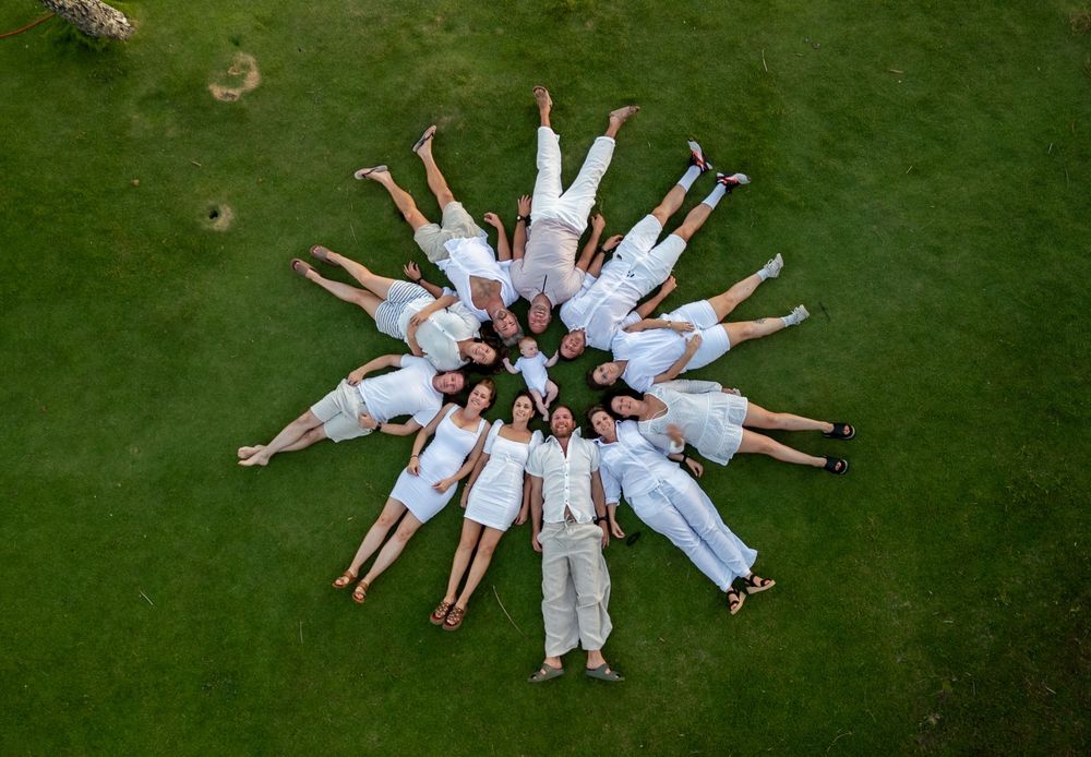 Aerial view of people wearing white outfits lying on green grass in a circular formation creating a star pattern.