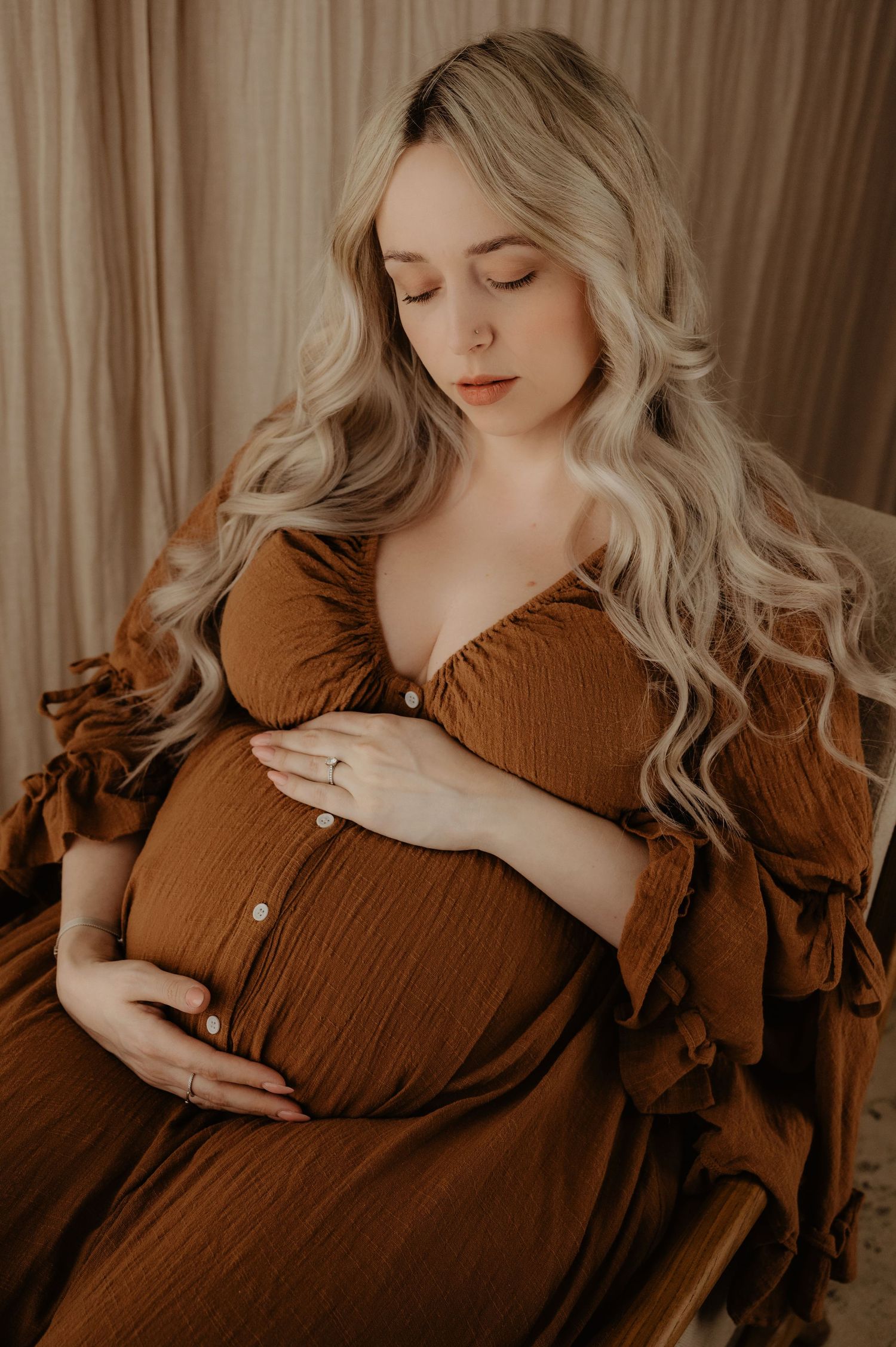 Expecting mother in brown dress cradles her baby bump in ethereal maternity portrait.