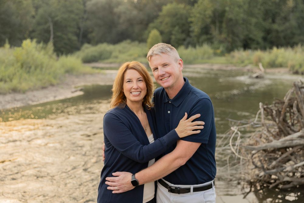 married couple hugging each other and smiling for a photo in front of a river
