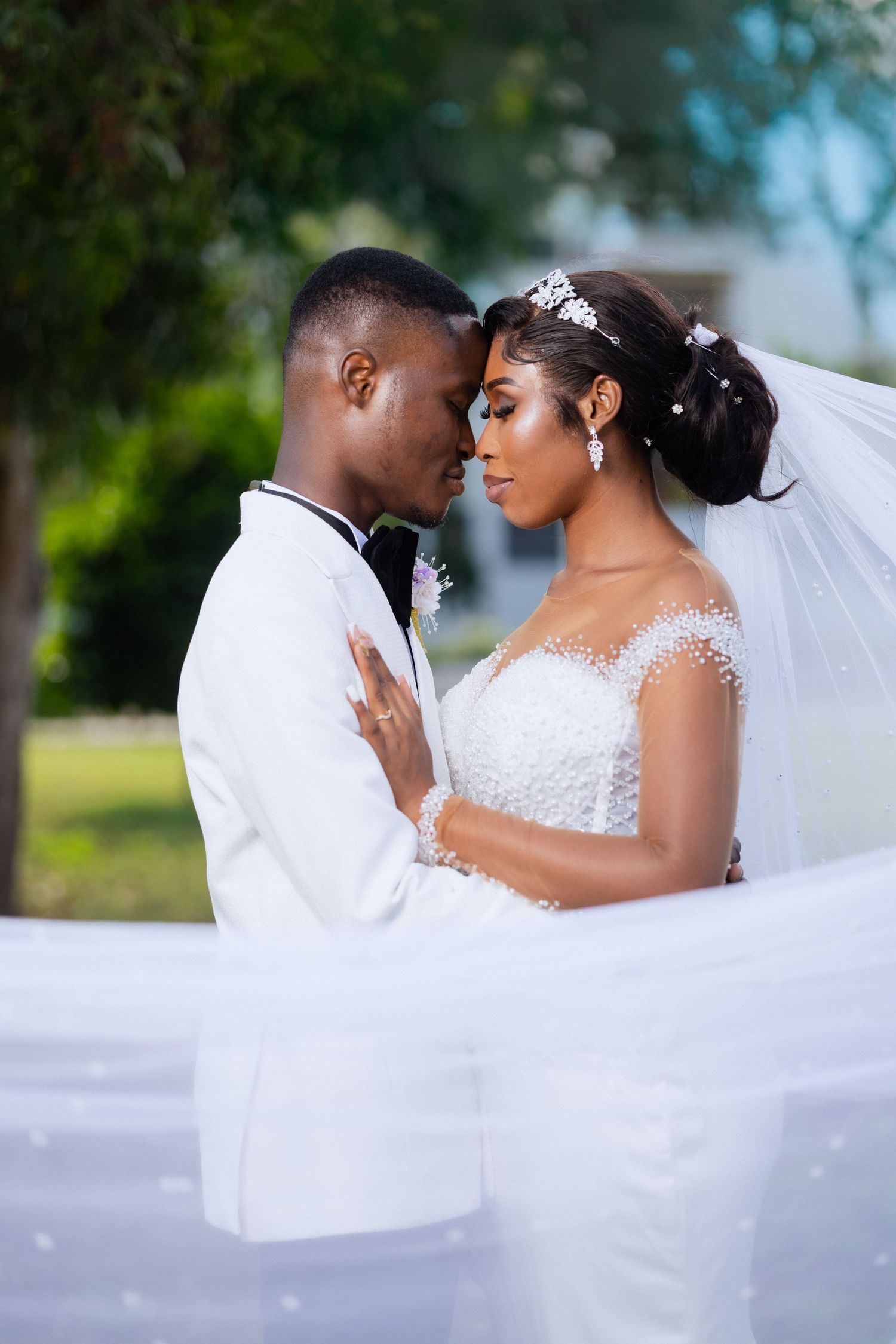 A romantic wedding couple shares intimate moments in a series of outdoor portraits with flowing white veil details.