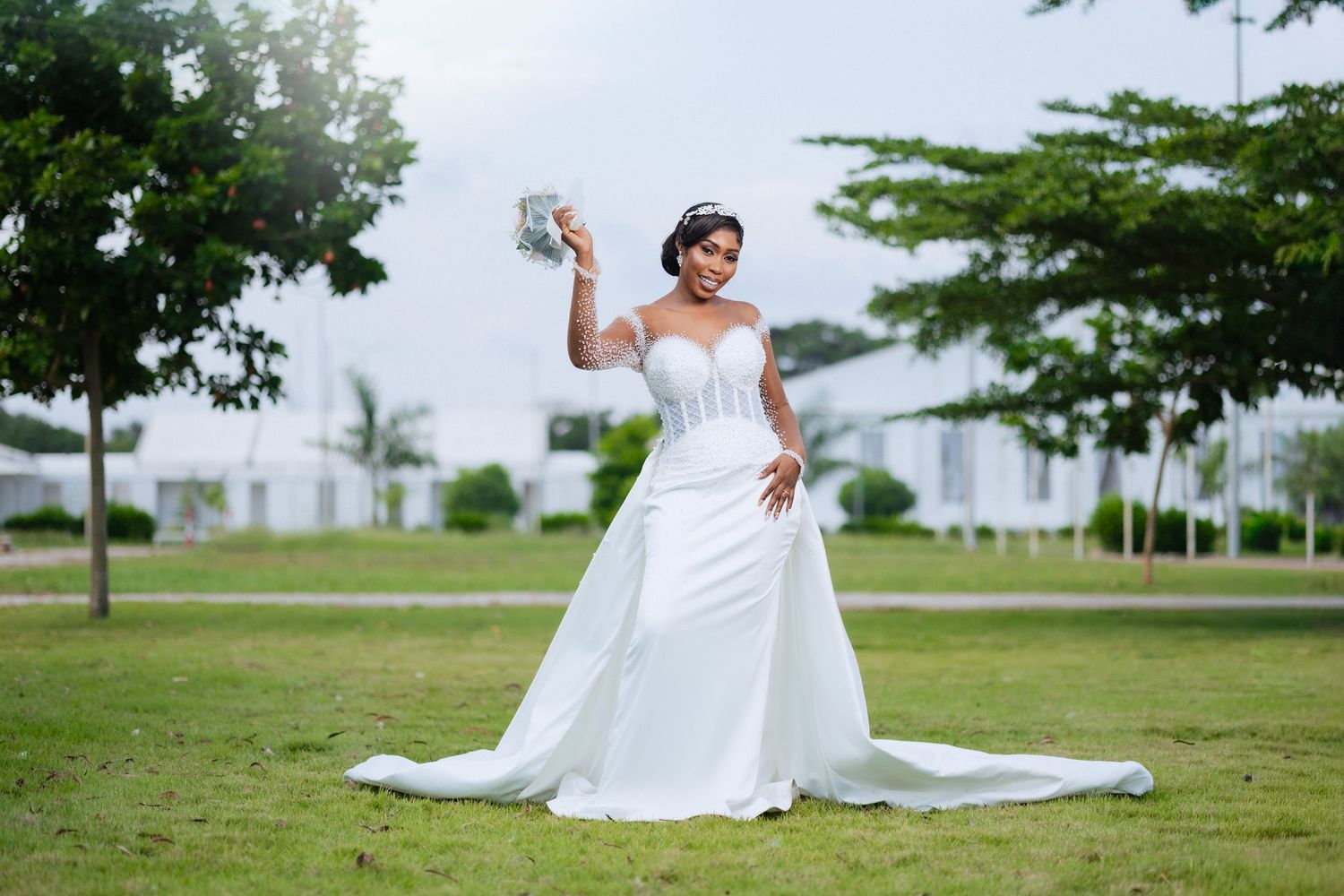 A flowing white wedding dress twirls gracefully in an outdoor garden setting with green trees in the background.